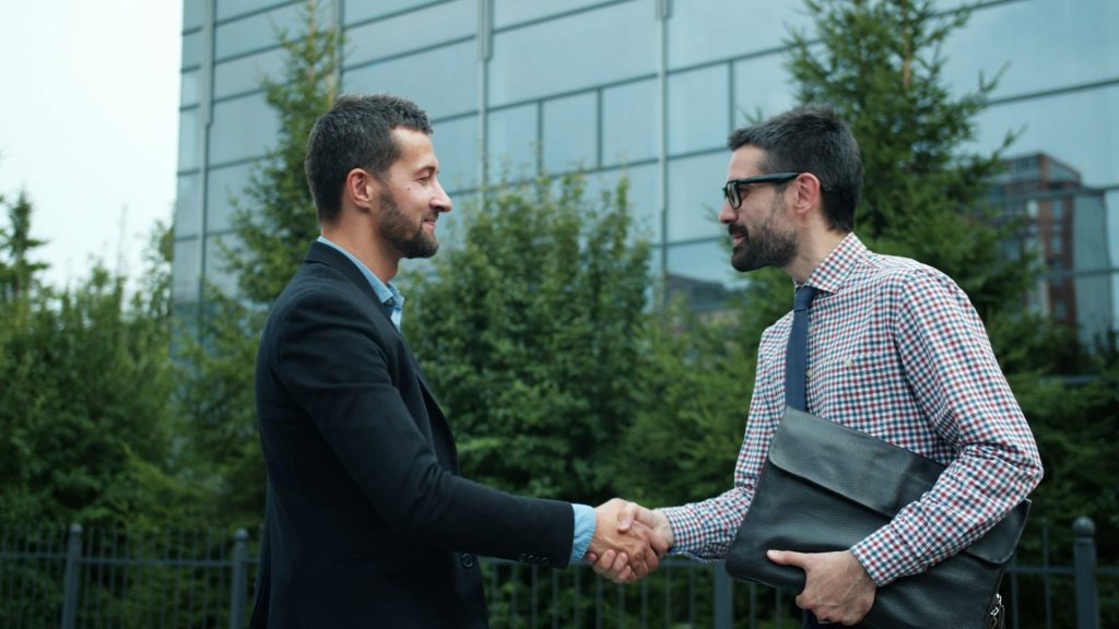 Two businessmen shaking hands outside modern building
