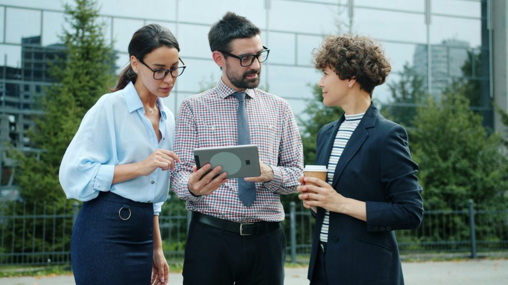 Three colleagues discussing a tablet outside an outdoor setting